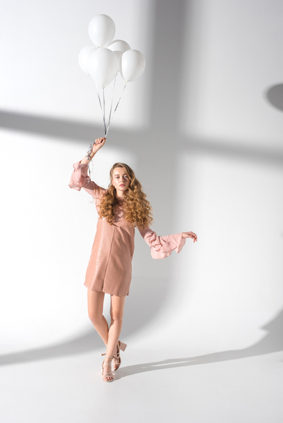beautiful woman in beige dress standing with hand up and holding bundle of balloons  - 写真・画像