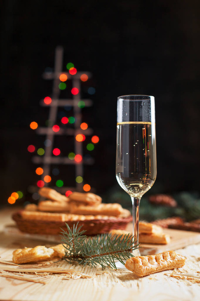 üveg pezsgővel, keksz, egy karácsonyfa és újévi fények egy újévi ünnepi asztal - Fotó, kép