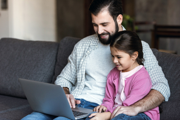 happy father with daughter sitting on couch and using laptop - Photo, image