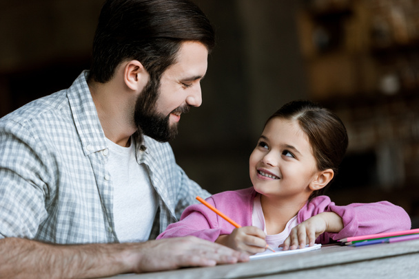 счастливый отец с маленькой дочкой, сидящей за столом и рисующей в альбоме дома
 - Фото, изображение