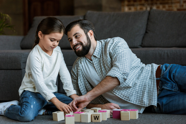 cheerful father with daughter making words by cubes with letters at home - Foto, Bild