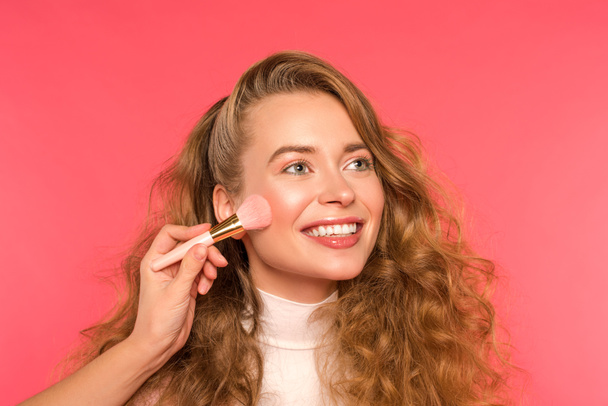 oříznutý obraz ženy dělá make-up pro usmívající se dívka izolované na červené - Fotografie, Obrázek