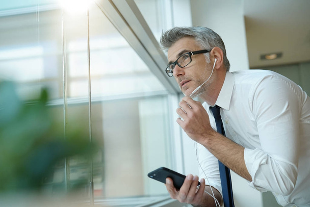 Businessman talking on phone in office, standing by window - Fotó, kép