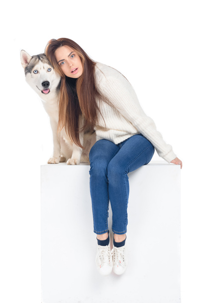 beautiful surprised girl sitting on white cube with husky dog, isolated on white - Fotoğraf, Görsel