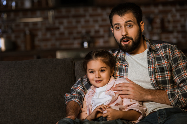 surprised father and daughter sitting on couch and watching tv at home - Photo, image