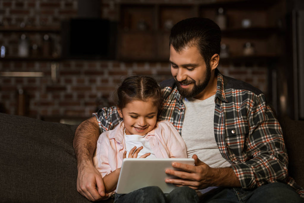 happy father with daughter sitting on couch and using tablet - Фото, зображення