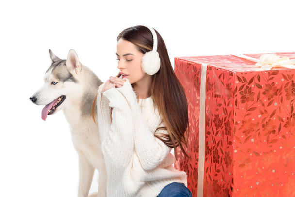 husky dog and tender woman in winter earmuffs with big christmas gift behind, isolated on white - Foto, imagen