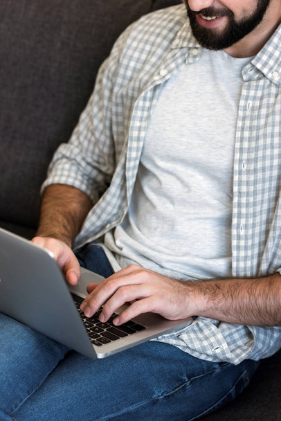 cropped image of man sitting on couch and using laptop - Foto, Bild