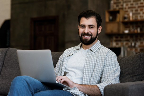 handsome man sitting on couch and using laptop - Foto, imagen