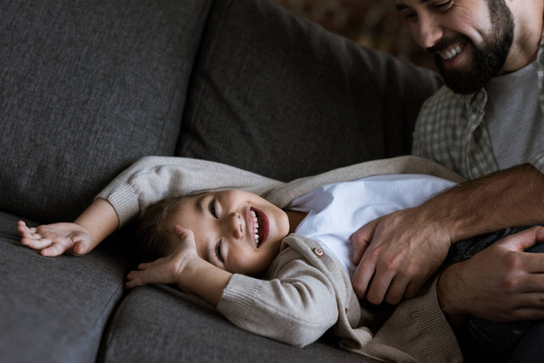 padre con hija acostada en el sofá, abrazando y riendo en casa
 - Foto, Imagen