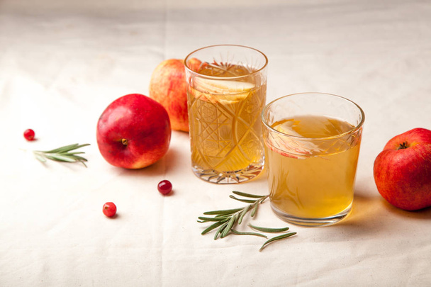 Two vintage glasses with apple cider on white background. Christmas beverages concept. Two red apples and rosemary sprig aside.  Warm backlight. Vertical composition. - Foto, imagen
