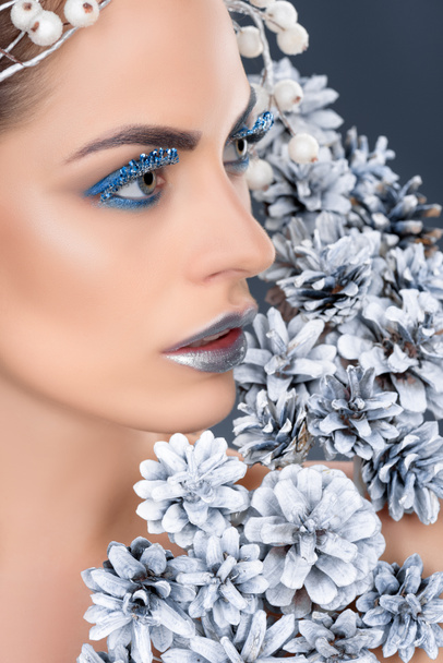 beautiful woman with christmas pine cones, winter makeup and glitter, isolated on grey - Φωτογραφία, εικόνα
