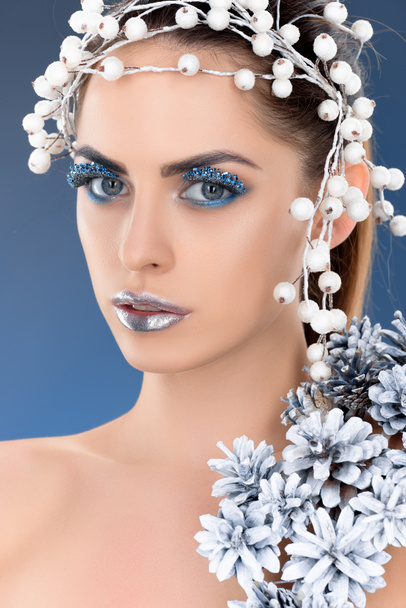 portrait of beautiful charming woman with hair accessory, christmas pine cones, winter makeup and glitter, isolated on blue - Foto, imagen