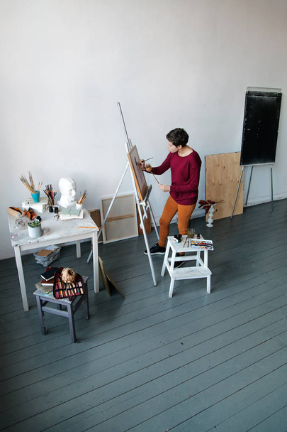 Female artist in her spacious white studio working with watercolor painting.  Natural lighting. Disclosure of creativity concept. Vertical composition with copy space - Fotoğraf, Görsel