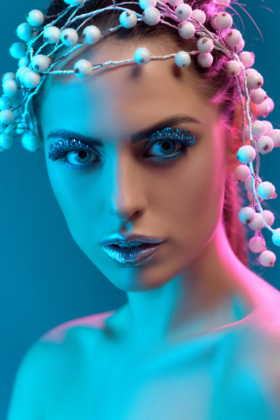 portrait of attractive model with hair accessory, winter makeup and glitter posing for fashion shoot, isolated on blue - Fotoğraf, Görsel