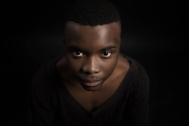 Headshot of serious confident young dark-skinned male standing isolated against black studiobackground. - Foto, imagen
