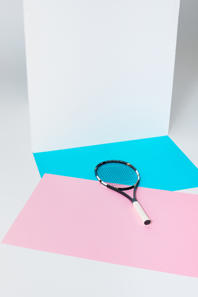 ξαπλωμένη σε μπλε και ροζ χαρτιά σε λευκό τοίχο ρακέτα του τένις - Φωτογραφία, εικόνα