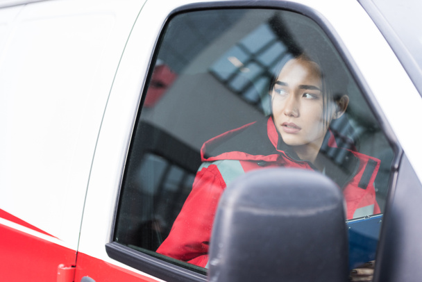 молодая азиатская женщина-парамедик сидит в машине скорой помощи и смотрит в сторону
 - Фото, изображение