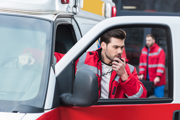 jóképű férfi paramedic beszél a hordozható rádió és állandó közel mentő - Fotó, kép