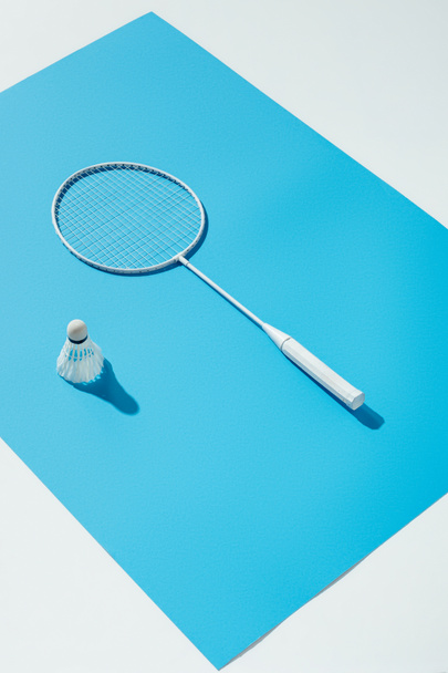 Badmintonschläger und Federball auf blauem Papier liegend, isoliert auf weißem - Foto, Bild