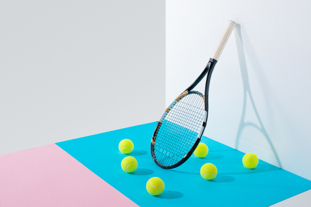 pelotas de tenis amarillas sobre papeles azules y rosados y raqueta de tenis en pared blanca
 - Foto, imagen