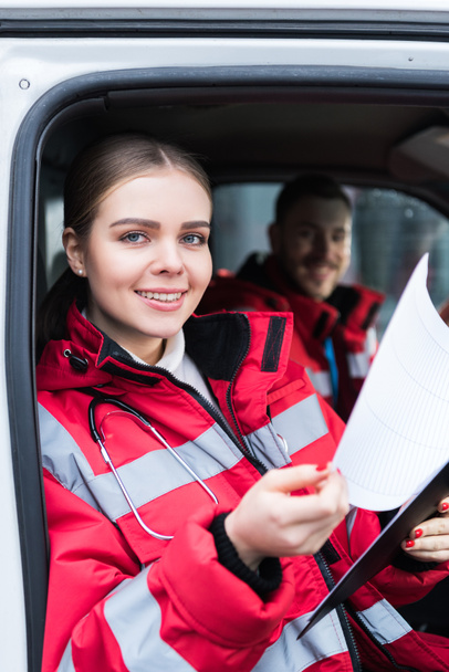 smiling young female paramedic holding clipboard and looking at camera - Фото, зображення
