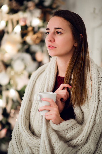 Young woman relaxing with a mug of coffee as she cuddles up in warm blanket on ancient commode. Her eyes closed and serene expression - Фото, изображение