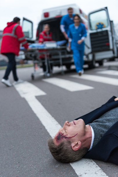 Οι γιατροί που τρέχει σε τραυματίες μέσης ηλικίας άνθρωπο που βρίσκεται σε έναν δρόμο  - Φωτογραφία, εικόνα