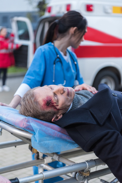 female doctor moving wounded mature man on ambulance stretcher - Fotó, kép