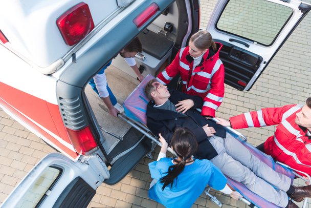 visão aérea da equipe paramédica que move o homem ferido na maca da ambulância no carro
 - Foto, Imagem