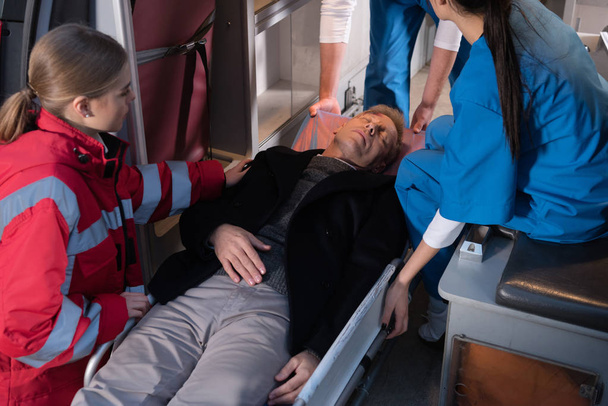 rajattu kuva ensihoitajista siirtämässä tajutonta miestä ambulanssiin
 - Valokuva, kuva