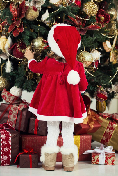 Merry Christmas and Happy Holidays. Cute little child girl is decorating the Christmas tree indoors. - Foto, Imagem