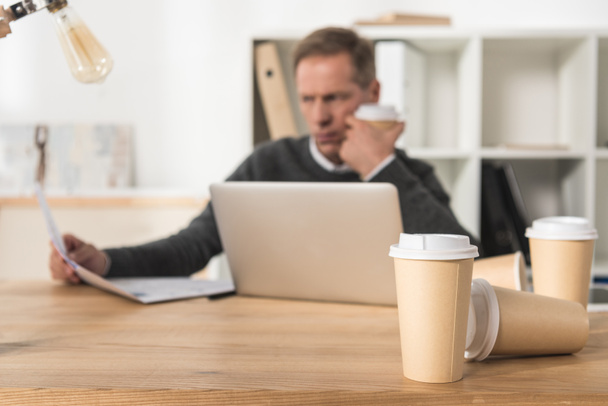 κουρασμένος επιχειρηματίας μέσης ηλικίας συνεργάζεται με το laptop και να πίνουν πολύ καφέ - Φωτογραφία, εικόνα