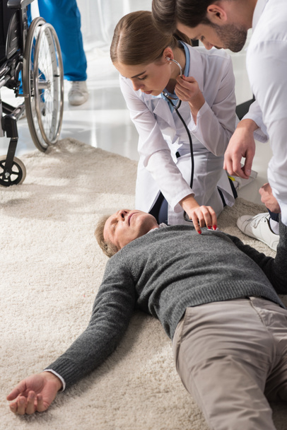 médico feminino verificando inconsciente homem de meia-idade palpitação com estetoscópio
   - Foto, Imagem