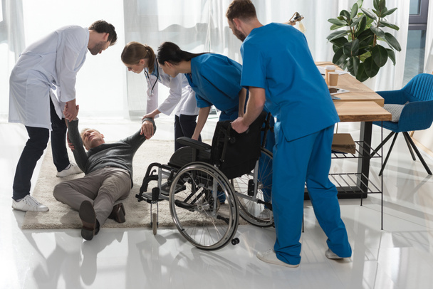 médicos ayudando cayó hombre maduro para sentarse en silla de ruedas
 - Foto, Imagen
