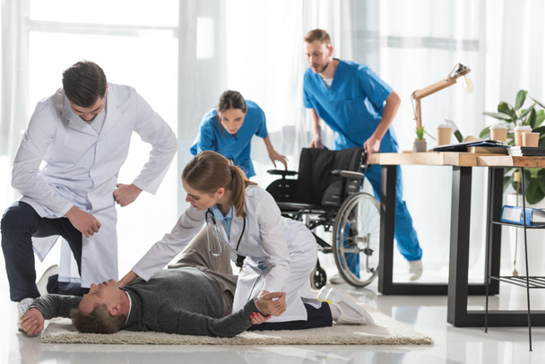νέοι γιατροί έλεγχος παλμό της ασυνείδητης άνθρωπο που λέει ψέματα σε ένα πάτωμα στο νοσοκομείο - Φωτογραφία, εικόνα