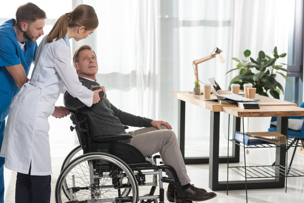 Ärztin spricht mit reifem Mann im Rollstuhl - Foto, Bild