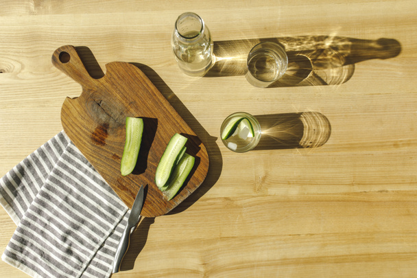 top view of cut cucumbers and antioxidant water on wooden surface  - Foto, Bild