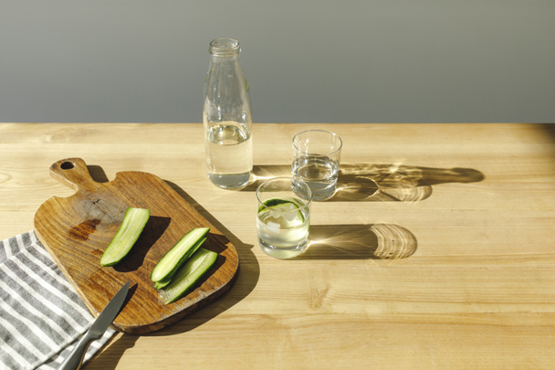 pepinos cortados sobre tabla de madera y agua mineral sobre mesa de madera
  - Foto, Imagen