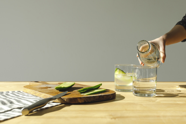 immagine ritagliata di donna versando acqua in bicchieri con cetrioli
 - Foto, immagini