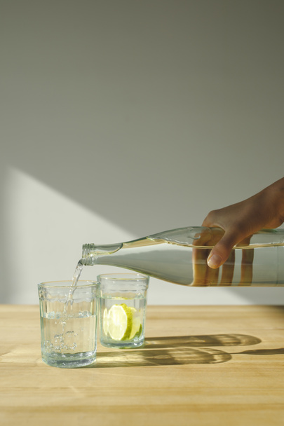 ořízne obraz žena nalití vody z láhve do průhledného skla  - Fotografie, Obrázek
