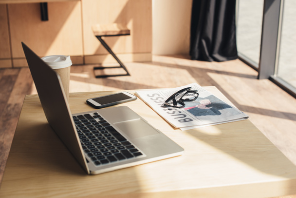 ноутбук, смартфон, очки и деловая газета на столе в кафе
 - Фото, изображение