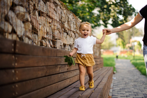 Kaunis pieni tyttö kävelee penkillä äidin käden avulla
 - Valokuva, kuva