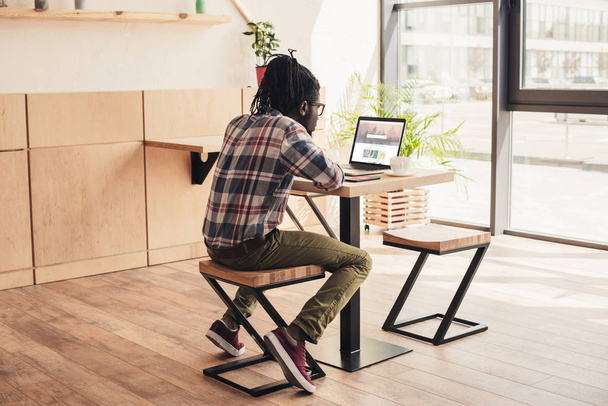 back view of african american man using laptop with shutterstock website in coffee shop - Foto, afbeelding