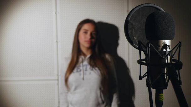 Όμορφη κοπέλα που τραγουδάει. Νεαρός τραγουδιστής τραγουδά σε ένα μικρόφωνο. Πορτρέτο κοντινό πλάνο του τραγουδιστή. Στούντιο ηχογράφησης. Καταγραφή σε οι τραγουδιστές στούντιο - Φωτογραφία, εικόνα