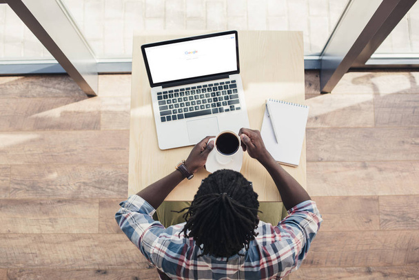 afro-amerikai ember iszik kávé és használ laptop-val google website felülnézete - Fotó, kép