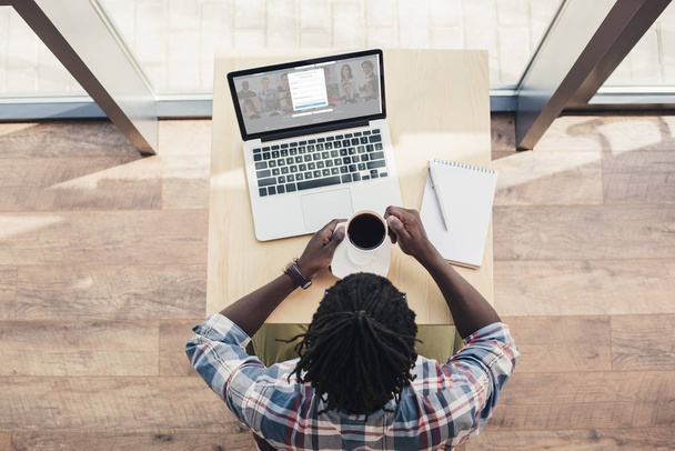 overhead view of african american man drinking coffee and using laptop with linkedin website - Photo, Image