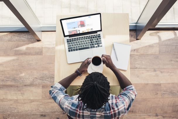 az afrikai-amerikai ember iszik kávé és használ laptop-val ebay weboldal felülnézeti - Fotó, kép