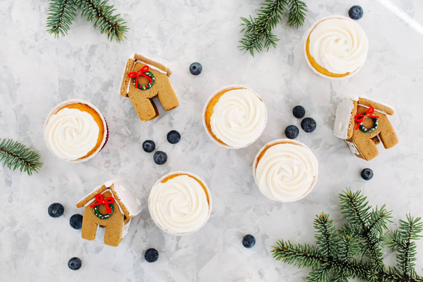 cupcakes with cream, gingerbreads of house shape and fir twigs on light marble background  - Φωτογραφία, εικόνα