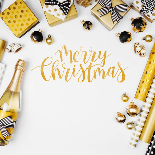 flat lay of champagne bottle, presents and golden wrapping paper rolls on white background. Merry Christmas text  - Foto, Bild